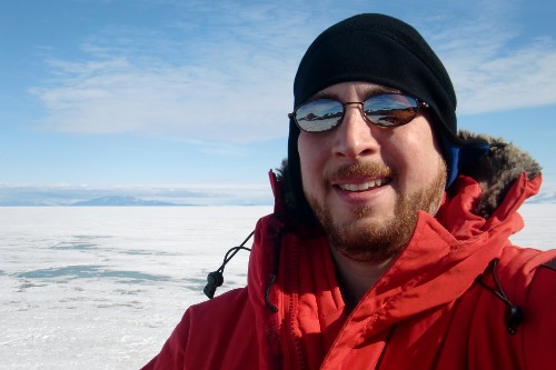 Selfie photograph taken at Hut Point.  In the background across the Ross Ice Shelf is Mt. Discovery (far left, and partly hidden by clouds) with the hills of Brown Peninsula.