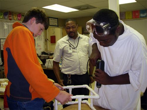 Mr. Cooper is overseeing Michael  and Rashad drill holes in the PVC  pipe pieces of our ROV frame.