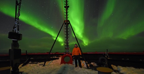 Bill Schmoker poses in front on a display of aurora aboard the USCGC Healy in the north Chukchi Sea