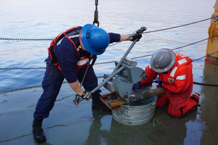 Caitlin Meadows and members of the Coast Guard empty the mud from the grab with a hose and spoon.