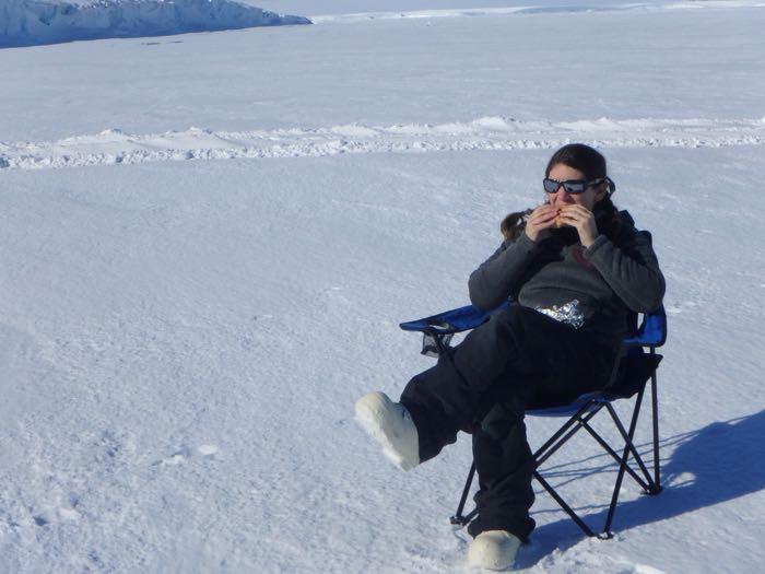 Amy Osborne in a lawn chair eating a sandwich on the sea ice.