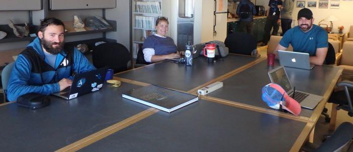 Three people sitting around a table looking at their computers. 