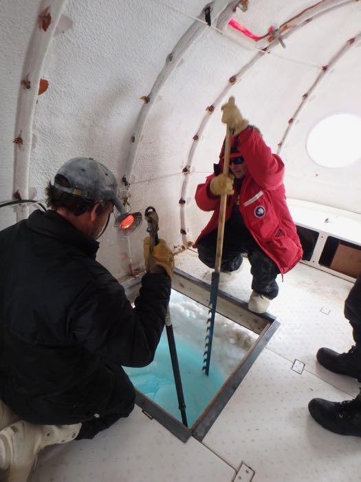 Two people clearing ice out of a dive hole