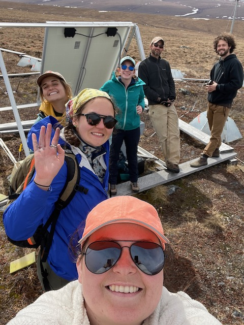 The whole team stands in front of the solar power box. 