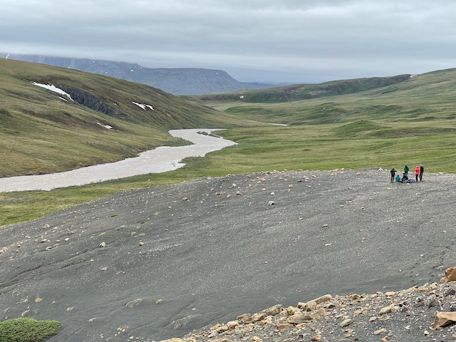 The group stands far in the distance next to a huge river. 