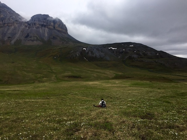 Liza sits in a field looking out at the mountains. 