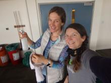 Amy Moran and Amy Osborne with spray bottles and the vacuum cleaning the lounges in the dorm.