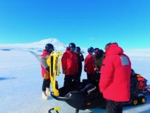 people on the sea ice looking at a snow machine with its hood up