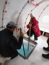 Two people clearing ice out of a dive hole