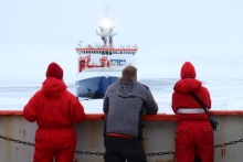 Three people look across the ice to a ship