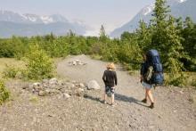 Two people hike on a glacial moraine, surrounded by cottonwood and spruce trees.