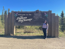 Liza stands in front of a big brown sign that says "Dalton Highway"