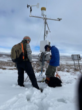 Sarah and Steve stand in front of a Meteorological Station. Steve looks at a laptop that is downloading information from the station.