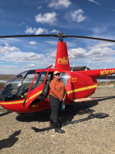 Liza stands in front of a red helicopter. 