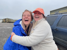 Liza and Sarah hug in front of a truck. 