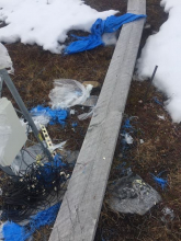 A boardwalk is littered with pieces of blue tarp, clear plastic, and black wires. 